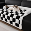 Cat lounging on a plush and thickened dog mat with a black and white checkered pattern on a black sofa.