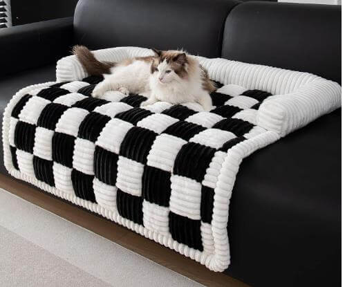 Cat lounging on a plush and thickened dog mat with a black and white checkered pattern on a black sofa.