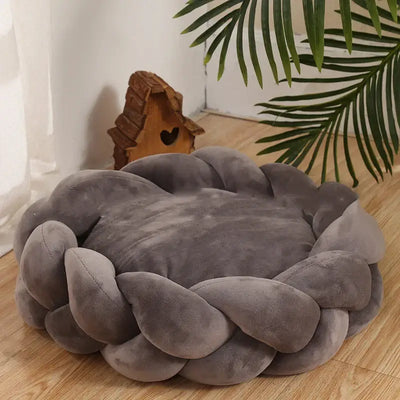 Cozy handmade knit pet bed in gray, perfect for cats and dogs, surrounded by plush braids, placed near a decorative house.