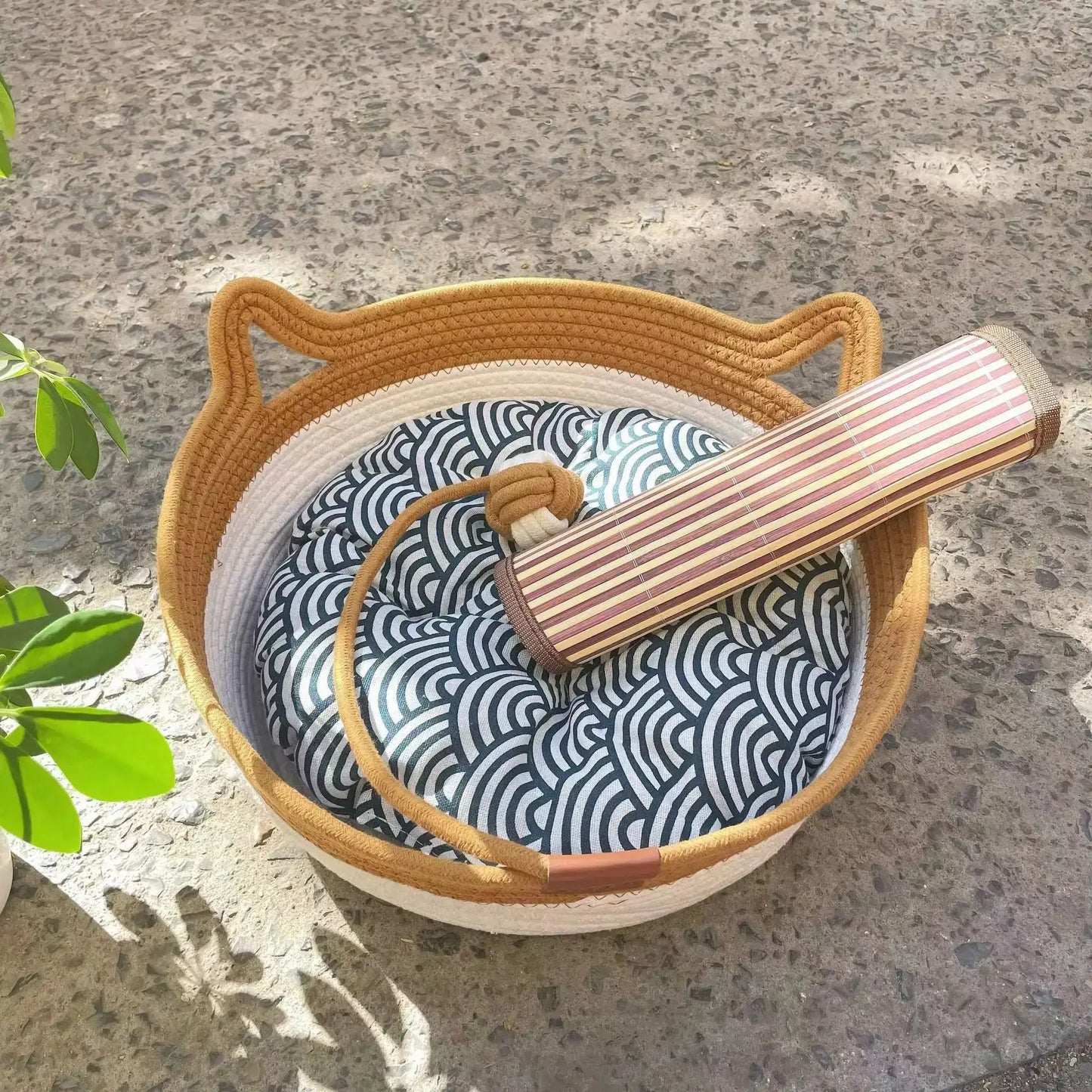 Natural rattan cat bed with washable basket and patterned cushion, placed outdoors on a stone surface.