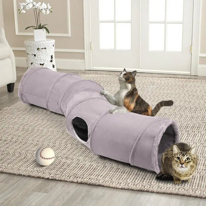 Two cats playing in a grey collapsible cat tunnel on a patterned rug with a ball nearby in a living room.